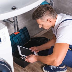 adult-repairman-sitting-on-floor-and-using-digital-tablet-while-repairing-sink-at-bathroom.jpg